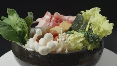 A Pot Of Shabu Ingredients Spinning Around On A White Table On Black Background