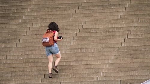 Woman Climbs Stairs with Backpack and Camera