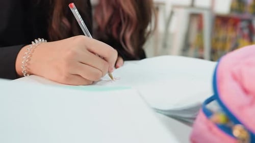 Teenage Student Writing in Notebook with Pen at Desk