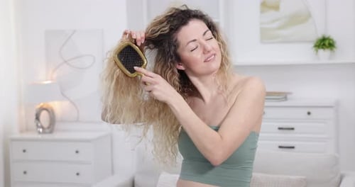 Unhappy woman trying to brush her tangled hair at home