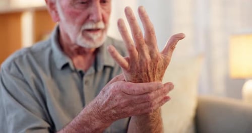 Senior Man Massages Aching Wrist Indoors
