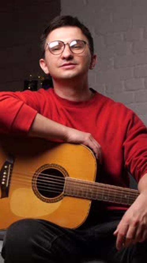 Vertical Video Portrait of a Young Man in Glasses with Guitar Looking at Camera