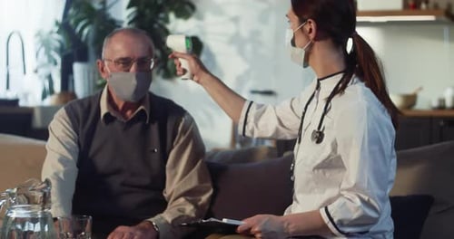 Young Doctor Woman in Lab Coat Takes Temperature of Happy Senior 6570 Caucasian Man at Home with
