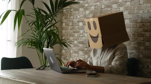 Person at Desk with Cardboard Box on Head