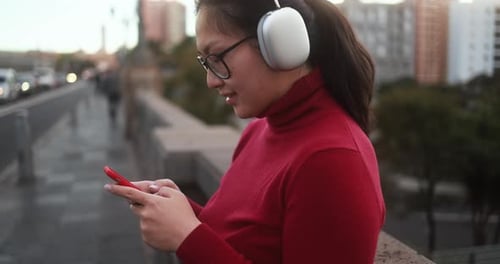 Young Woman Uses Phone With Headphones in City
