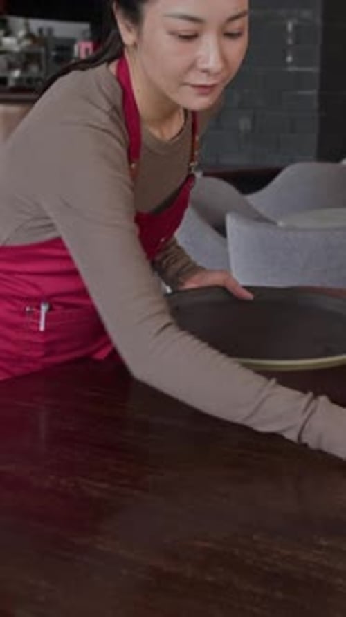 Vertical of Waitress Cleaning Tables in Cafe