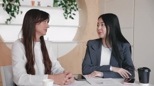 Friendly Woman in White Shirt Extending Hand Across Table While Colleague Hesitates Slightly with