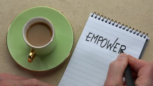 Empower word - man hand writing a note with a black marker in a spiral notebook, overhead view