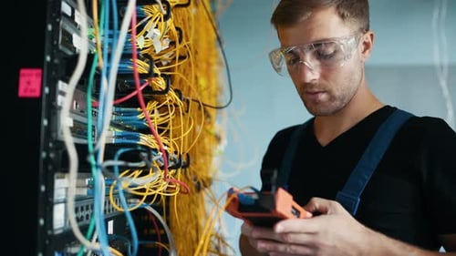 Young man in uniform testing internet equipment by using special device in server room