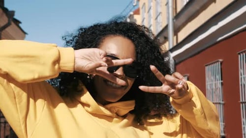 Smiling Woman Making Peace Signs on City Street