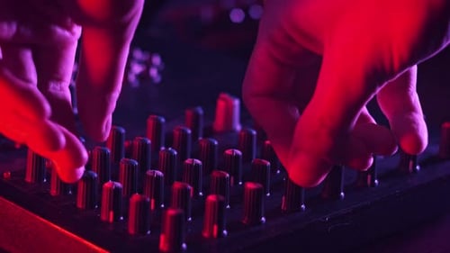 Male Hand Adjusting Buttons on Audio Mixer in Neon Light CloseUp