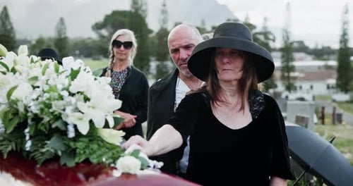 Coffin, flowers and senior couple at funeral, burial service or hug for comfort at cemetery