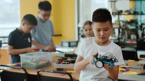 Ein Schüler erkundet den zusammengebauten Roboter und lächelt in einer Klasse mit den anderen Kindern an einer Robotik
