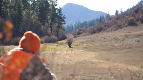 Hunter waits in field with mountain in background. Deep Background Focus. 4K