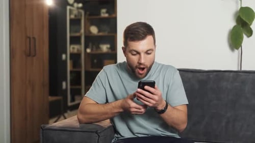 Man on Sofa Reacts to Phone Screen News