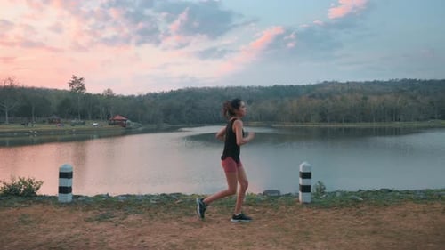 Woman Runs by Tropical Lake During Sunrise