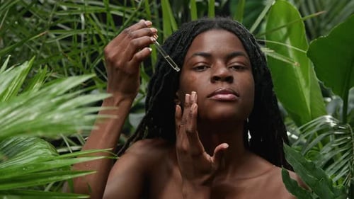Portrait of Young Black Woman Applying Serum to Face in Jungle Forest