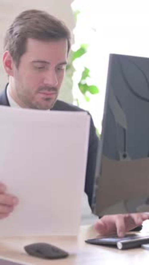 Focused Man Reads Documents at Office Desk