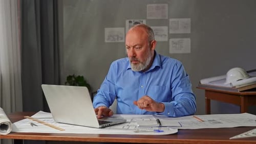 An Architect Sits in an Office at a Desk with Blueprints