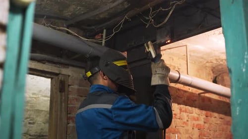 Close Up Side Shot of Professional Welder in Safety Suit and Protective Mask Welds Metal Door Using