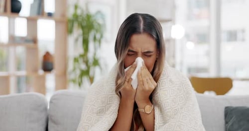 Young Woman Blowing Nose Wrapped in Blanket on Couch