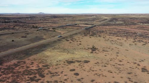 Cars driving over a Highway between brown and orange desert in the state Arizona on partly cloudy da