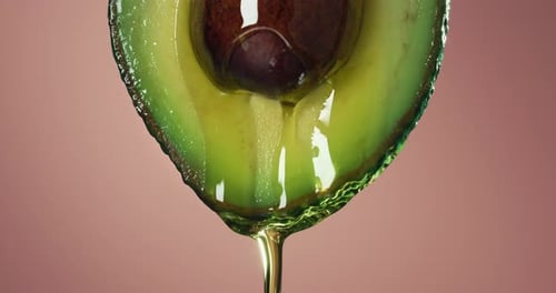 Cinematic macro shot of half raw fresh organic vegan green avocado fruit with oil stream isolated