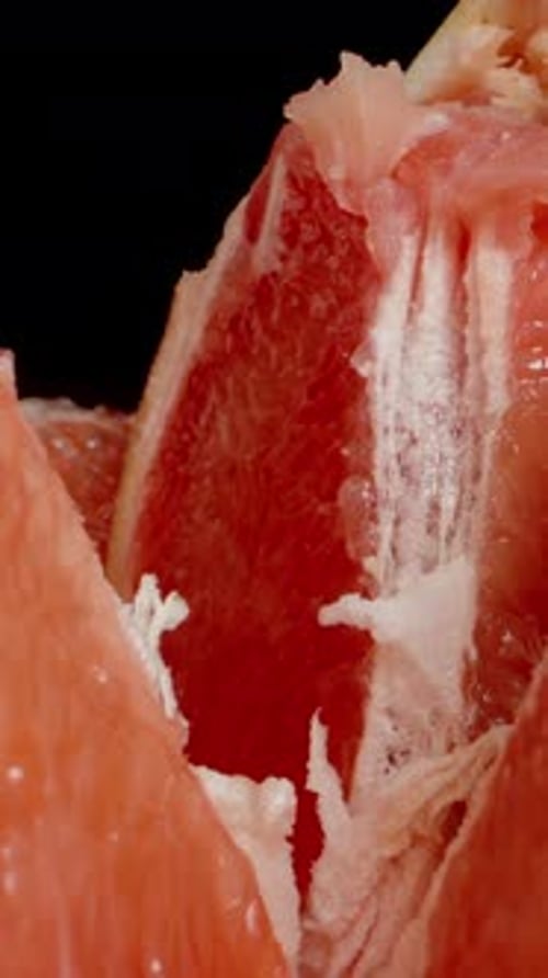 Vertical video. The camera zooms into the inside of a broken apart grapefruit, capturing a macro sho