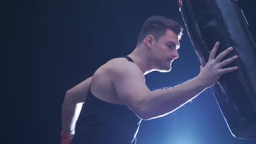Male boxer. Strong athlete hits the punching bag.