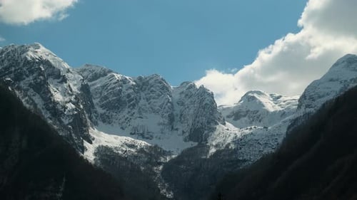 Thick white clouds flowing over snow-covered mountain tops, timelapse