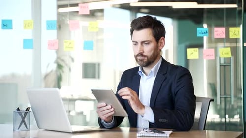 Portrait of smiling businessman using digital tablet sitting at desk at workplace in business office