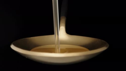 I pour yellow syrup on a golden spoon. Dolly slider extreme close-up. Laowa Probe