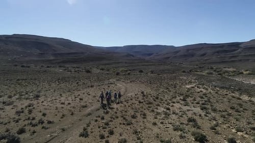 Aerial follows trekkers hiking in vast, barren, hilly desert landscape