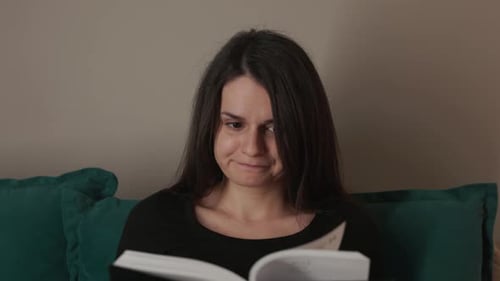 A Young Woman Seated on the Couch, Engrossed in Reading a Book - Close Up