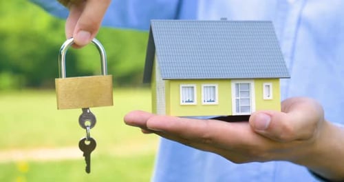 Realtor, broker, businessman is holding a small yellow house with keys and a lock, for sale, buyin