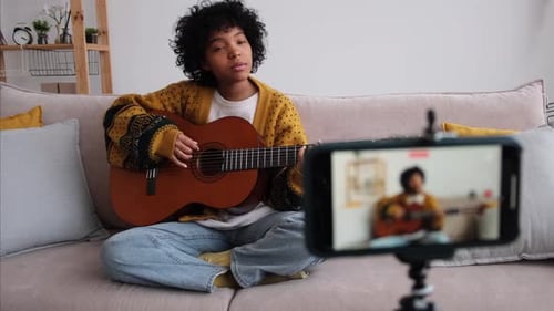 Young Woman Plays Guitar on Couch for Recording