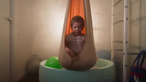 Boy in Beige Swing in Indoor Playroom