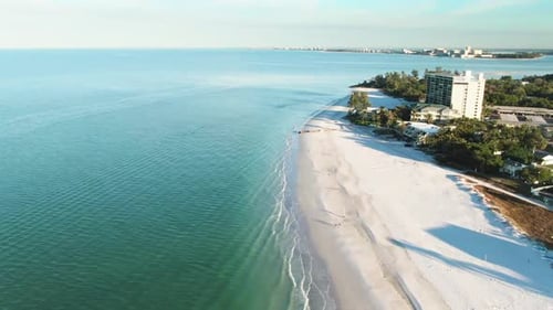 An aerial view of a pristine beach with turquoise waters and gentle waves lapping the shore. A small