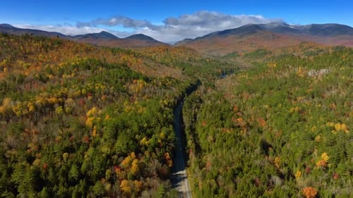 Thick woods covering the rocky landscape change colors in autumn. A highway crosses the forest