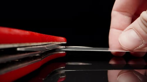 Rotes Klappmesser auf schwarzem Glas. Ich falte die Klinge zusammen. Dolly Slider extreme Nahaufnahme. Laowa-Sonde