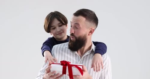Niño sorprende a su padre con un regalo sobre fondo gris claro