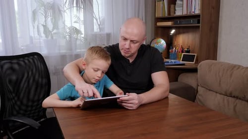 Joyful Father and Son are Looking at the Screen of the Tablet at Home