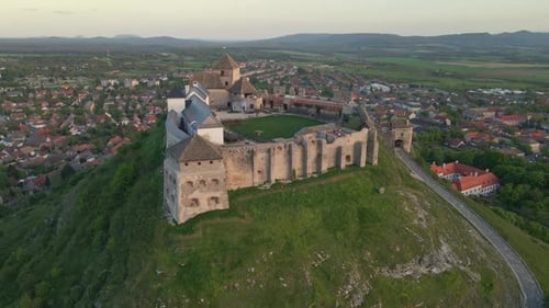 Aerial view of a medieval castle fortress standing a top of a hill, surrounded by a charming town an