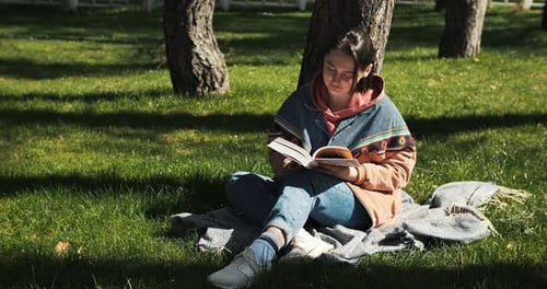 Portrait of Cheerful Young Woman Reading Book in the Park Reading Outside in Spring Sunlight Girl