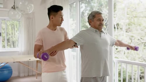Diverse male physiotherapist advising and determined senior man using dumbbells, in slow motion