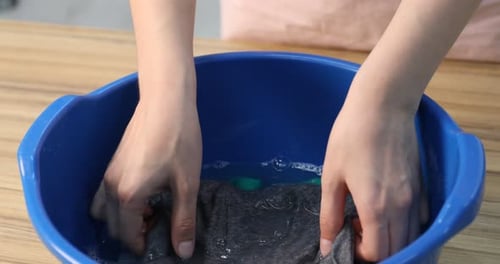 Woman washing baby clothes in basin on wooden table indoors, closeup