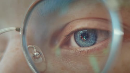 Gros plan d'un œil bleu vif, parcourant les graphiques des cryptomonnaies tard dans la nuit. Femme d'affaires concentrée.