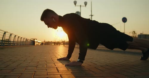 Young Athletic Man Works Out Doing Pushups on a City Street at Golden Sunset