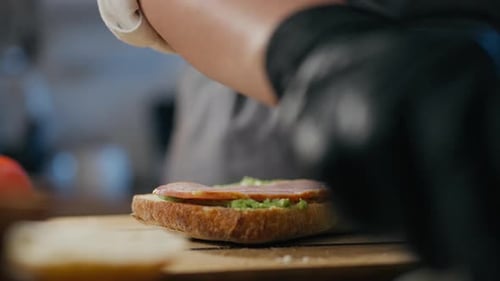 Cooking, chef baker concentrated Add pieces of bacon meat in an authentic sandwich bar. Close-up