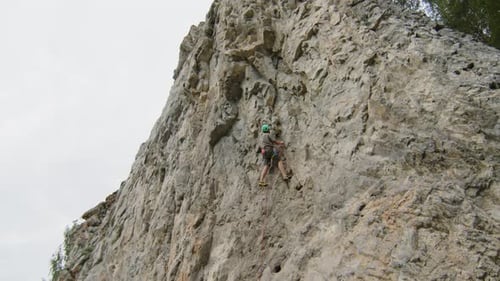 Mountain Climber Ascending Rock while Female Partner Holding Rope